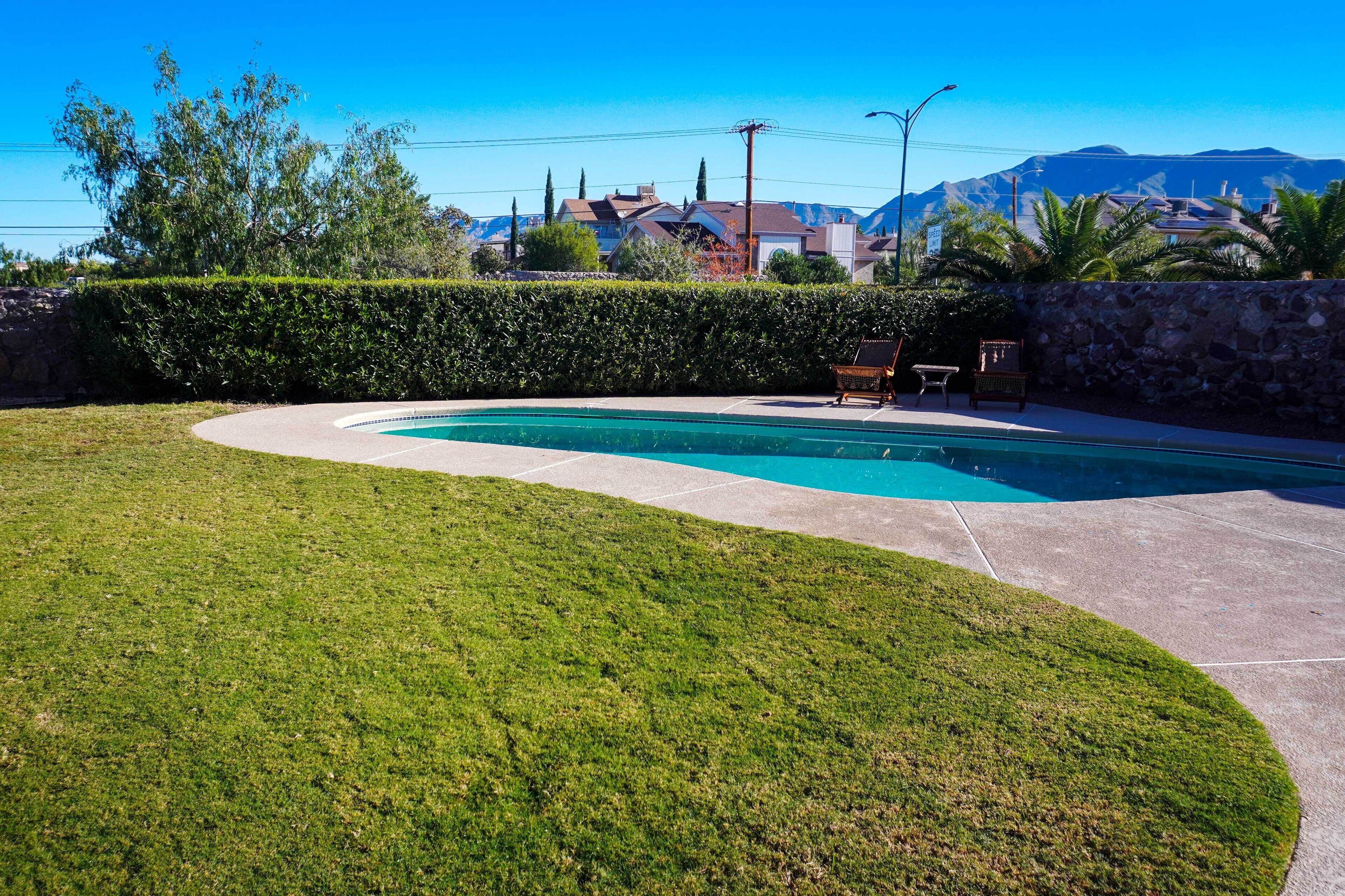 Piscina com borda curva, cercada por um gramado bem cuidado e uma parede de pedra.