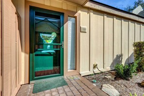 Une maison avec une porte verte, un petit jardin devant, un chemin en briques et une clôture en bois.