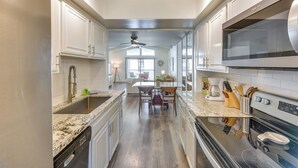 A modern kitchen with white cabinetry, a granite countertop, stainless steel appliances, and a dining area with a table and chairs.