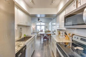 A modern kitchen with white cabinetry, a granite countertop, stainless steel appliances, and a dining area with a table and chairs. - Pool Access: Pet-friendly Palm Springs Condo (Palm Springs)