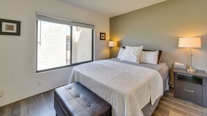 Een slaapkamer met een groot bed, een bankje, een nachtkastje en een raam met jaloezieën.