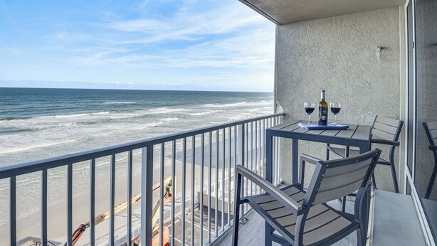 A balcony with a view of the ocean, a table with two wine glasses, and a chair. - Daytona Beach Retreat: Beach Access! (Daytona Beach Shores)