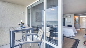 A balcony with a table and chairs, a bed, and a view of the sea. - Daytona Beach Retreat: Beach Access! (Daytona Beach Shores)