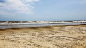 Une plage où l’on voit clairement les traces de pneus et où le ciel est dégagé.