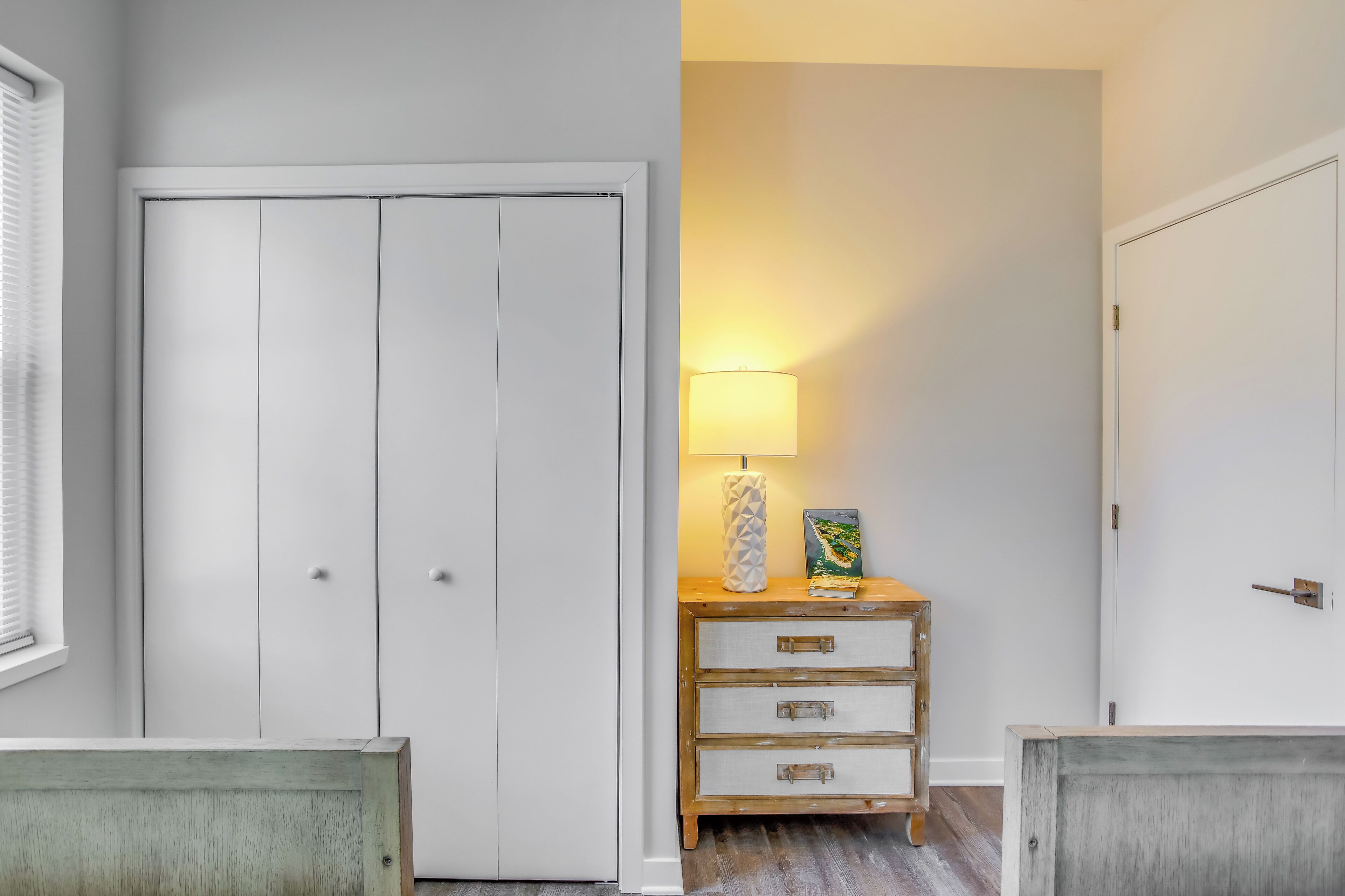 A hallway with a white wardrobe, a wooden nightstand with drawers, and a lamp.