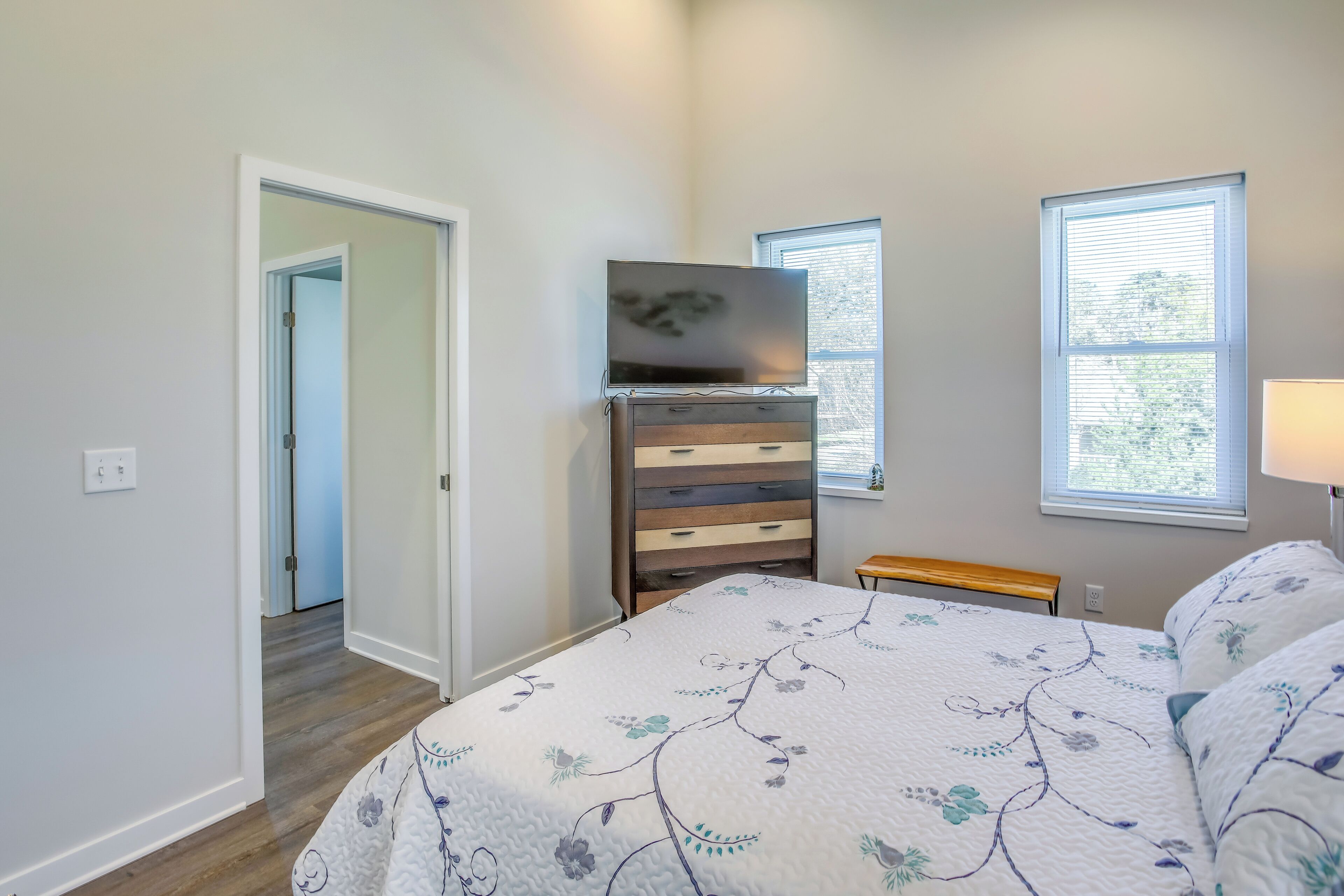 A bedroom with a bed, dresser, TV, and windows.