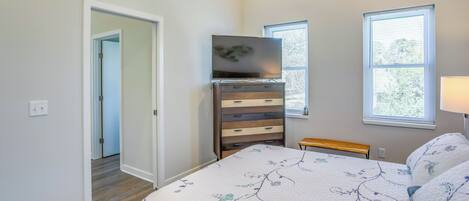 A bedroom with a bed, dresser, TV, and windows.