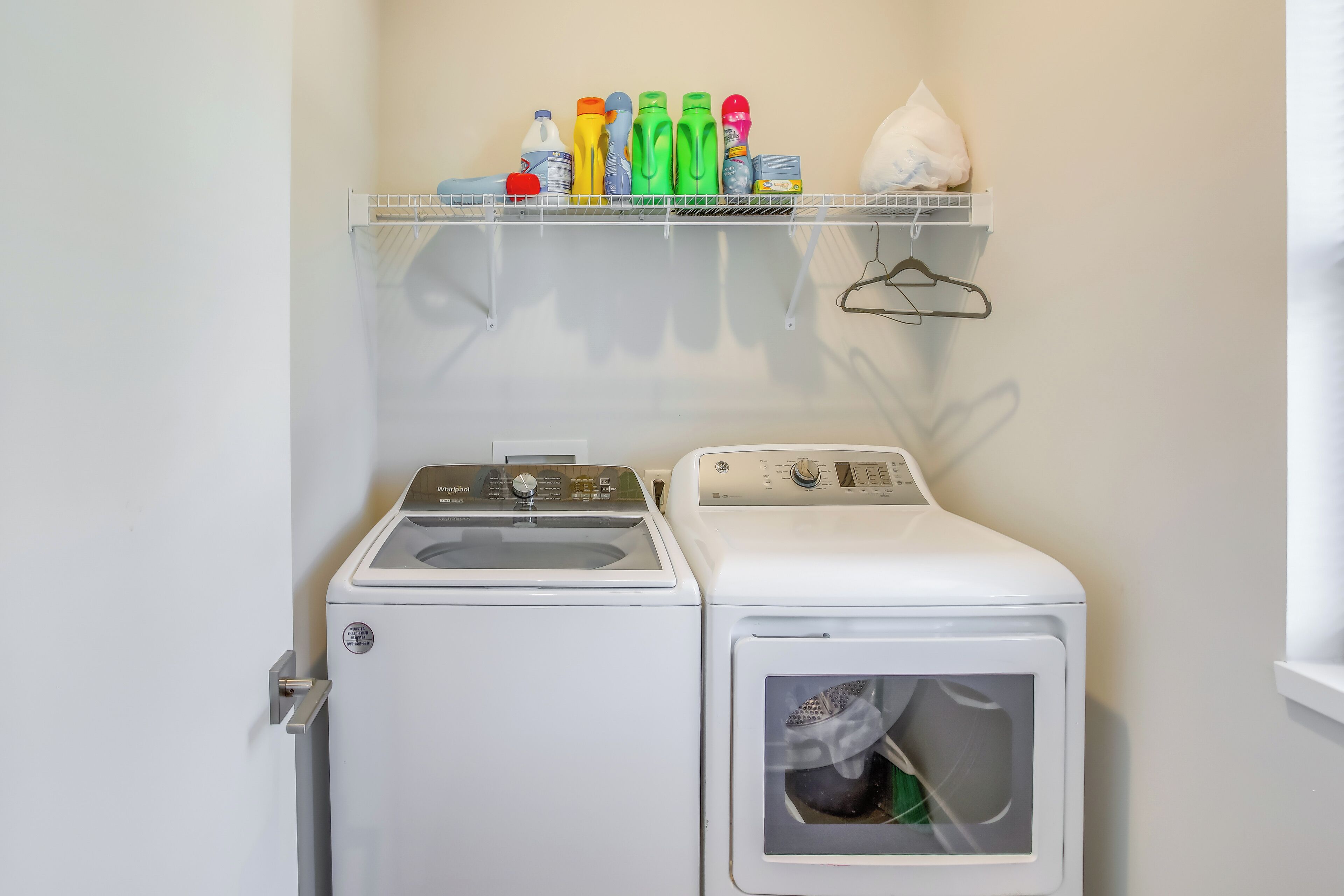 A laundry area with a washing machine and dryer, a shelf with cleaning supplies, and a hanging clothes rack.
