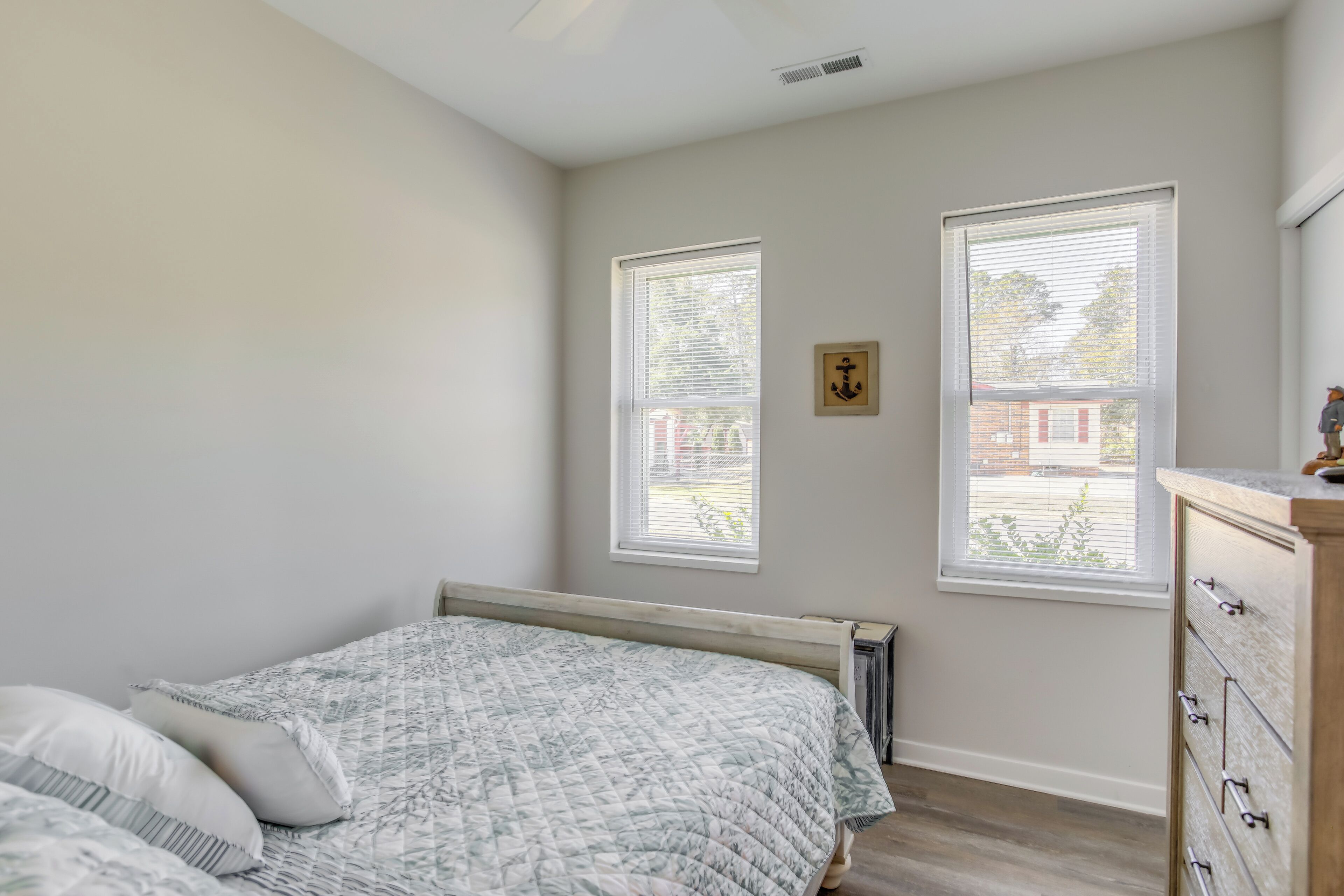 Une chambre à coucher avec un lit, deux fenêtres, un radiateur et une commode.