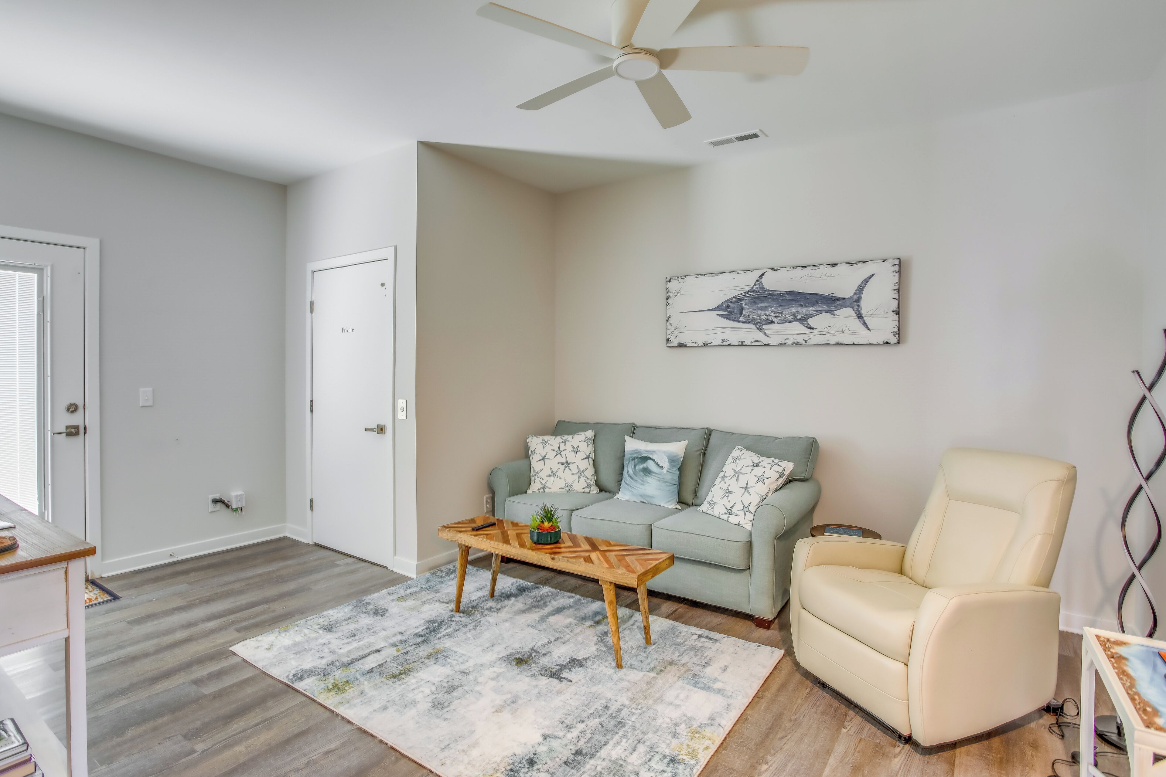 A living room with a light green sofa, a beige armchair, a wooden coffee table, and a ceiling fan.