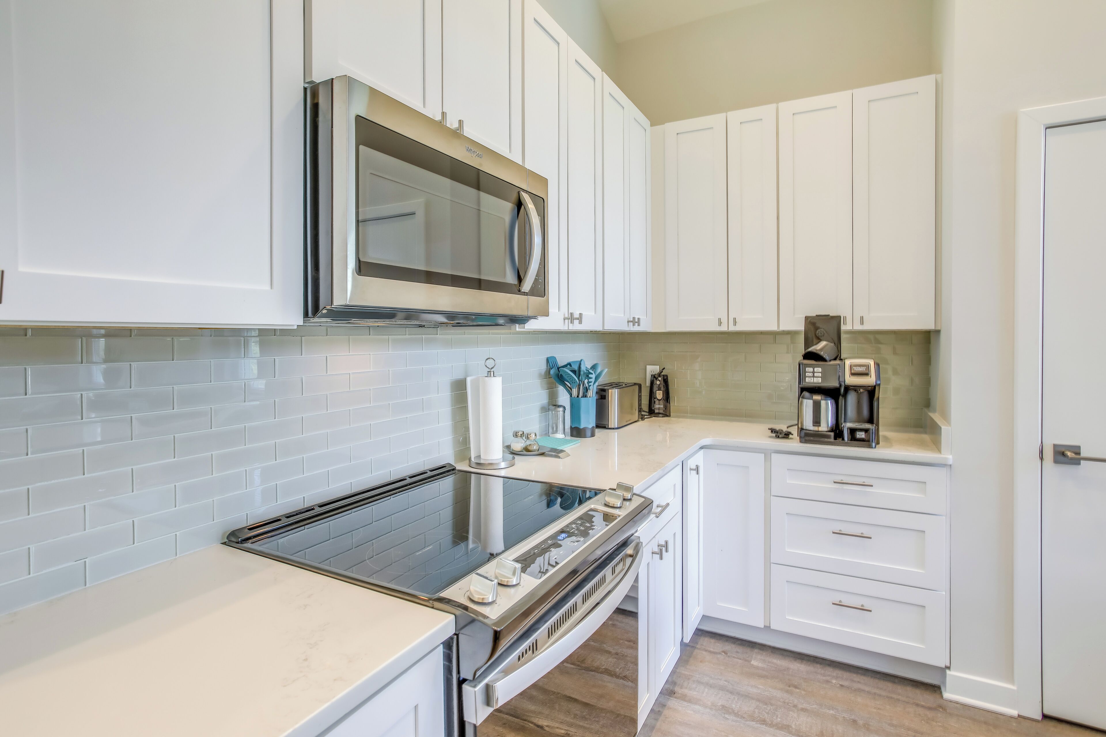 A modern kitchen with white cabinets, a stainless steel microwave, a built-in oven, and a coffee maker on the countertop.