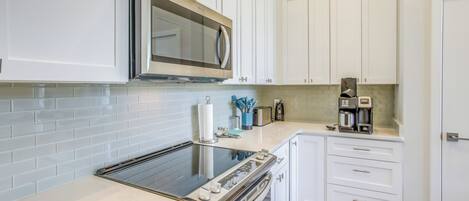A modern kitchen with white cabinets, a stainless steel microwave, a built-in oven, and a coffee maker on the countertop.