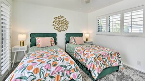 A bedroom with two beds, each with a floral bedspread, a ceiling fan, and a wall-mounted light fixture. - Furnished Patio + Pool Access: Palm Springs Condo (Palm Springs)