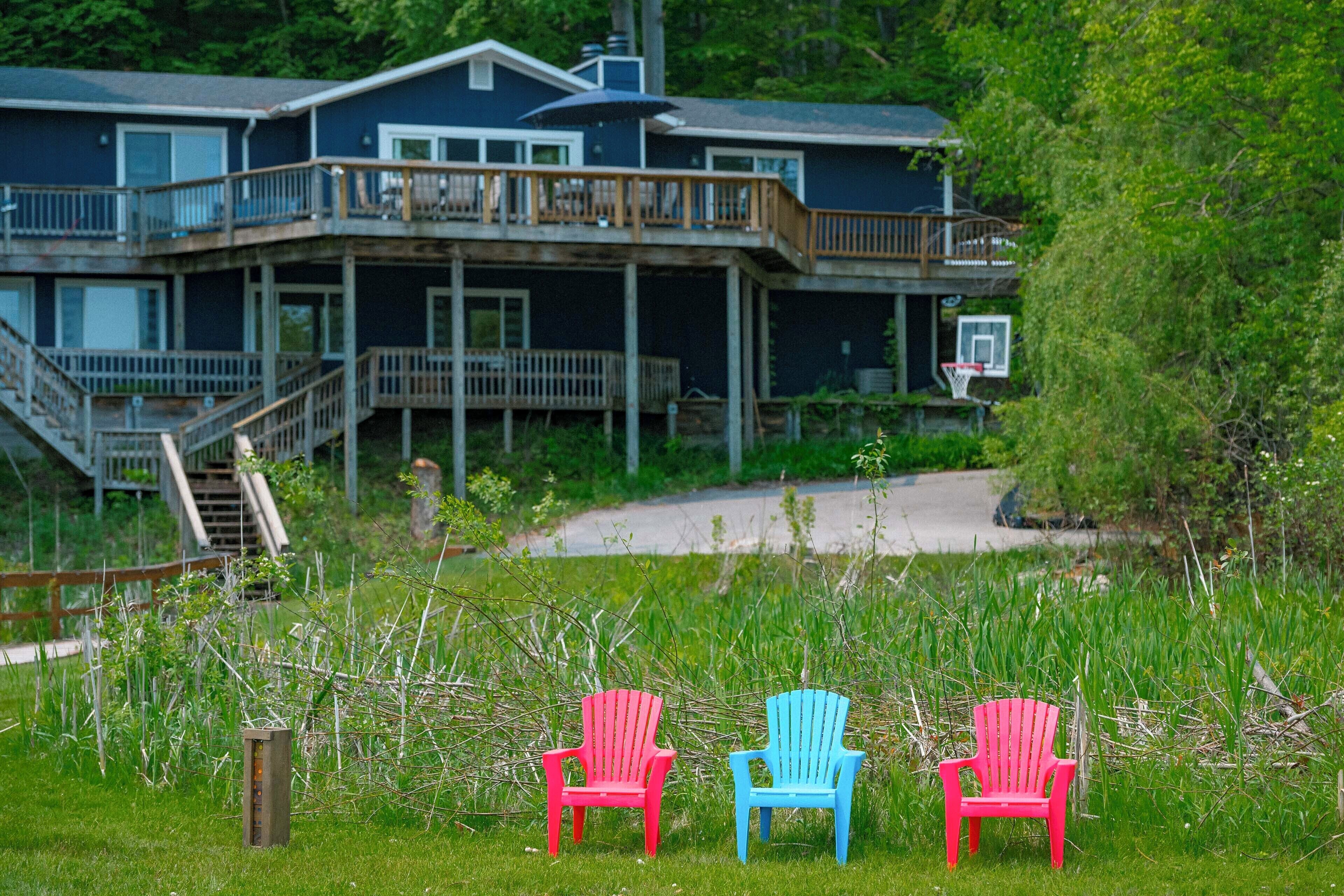 A two-story house with a deck and a basketball hoop. There are two colorful chairs in the foreground.