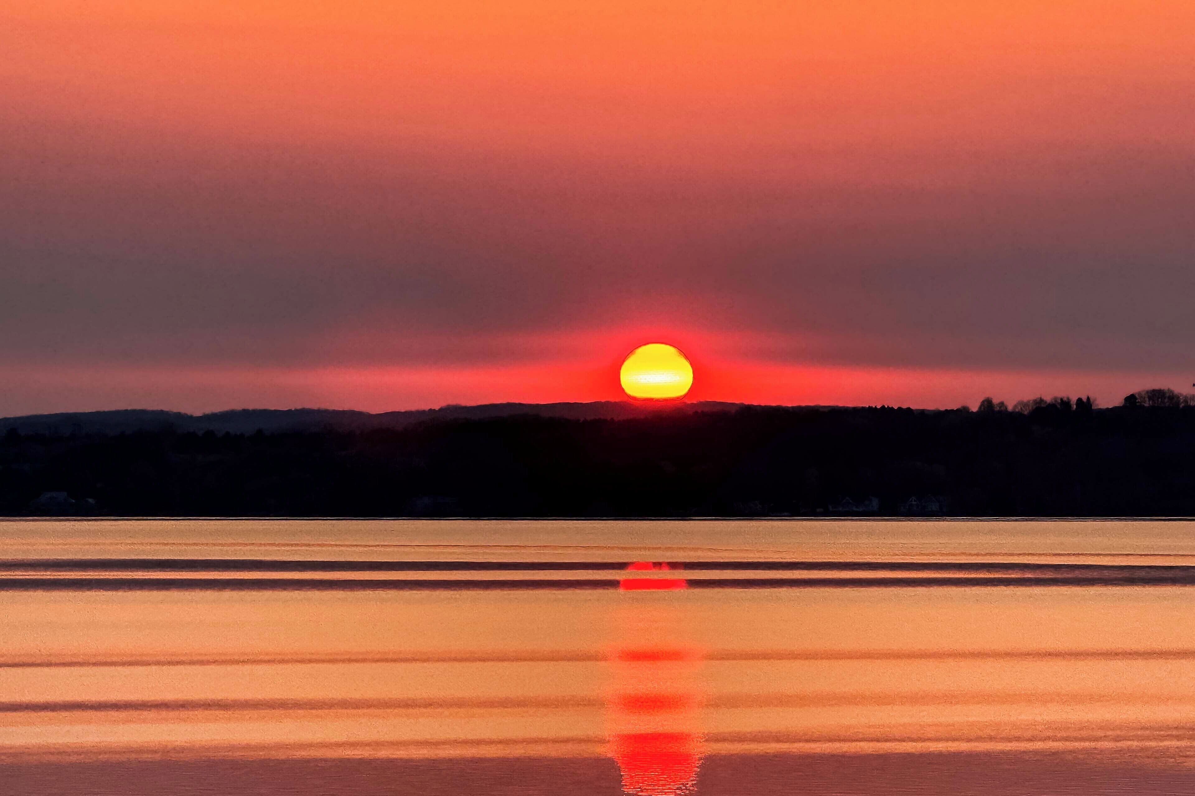 A sunset over a calm body of water with a silhouette of hills in the background.