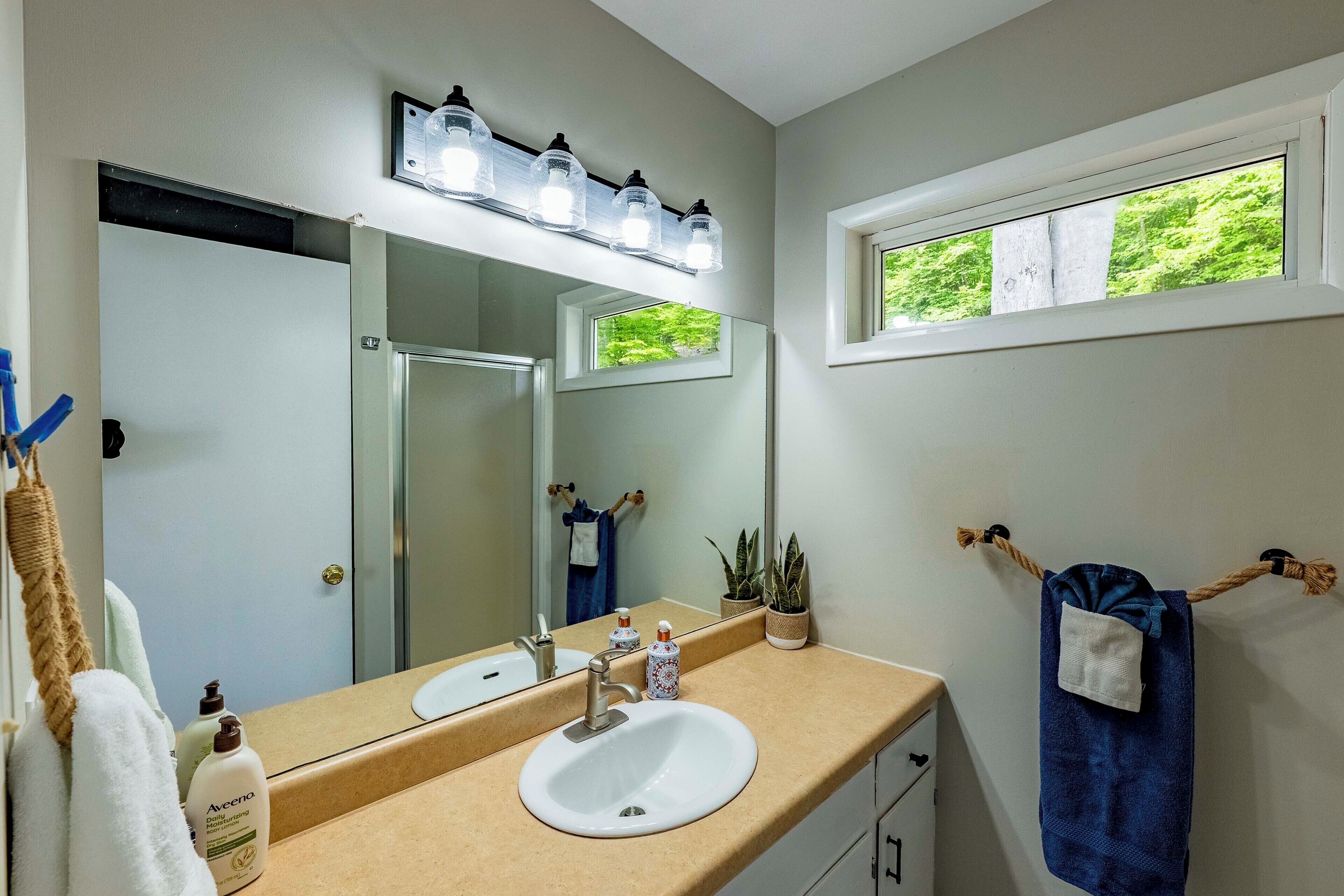 Un baño con un lavabo blanco, un espejo y una ventana con vistas a la vegetación.