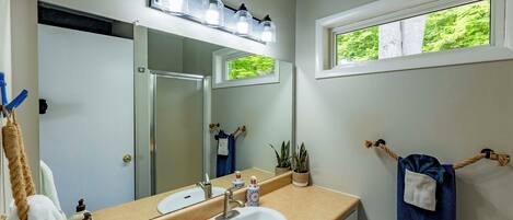 Un baño con un lavabo blanco, un espejo y una ventana con vistas a la vegetación.