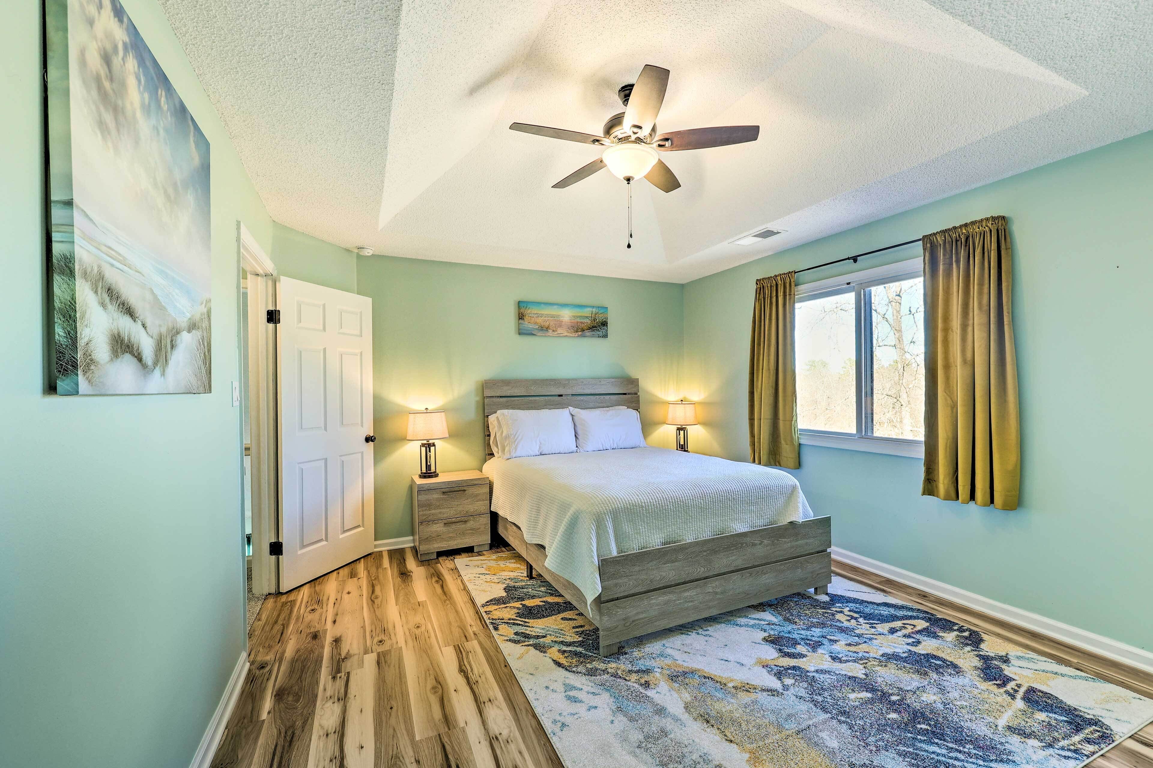 A bedroom with a bed, nightstands, a ceiling fan, a window with curtains, and a door.