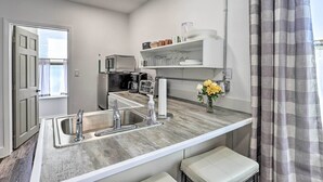 Een moderne keuken met een ingebouwde spoelbak, een magnetron en een koffieapparaat. Er is een klein plankje met drinkgerei en een vaas met bloemen.