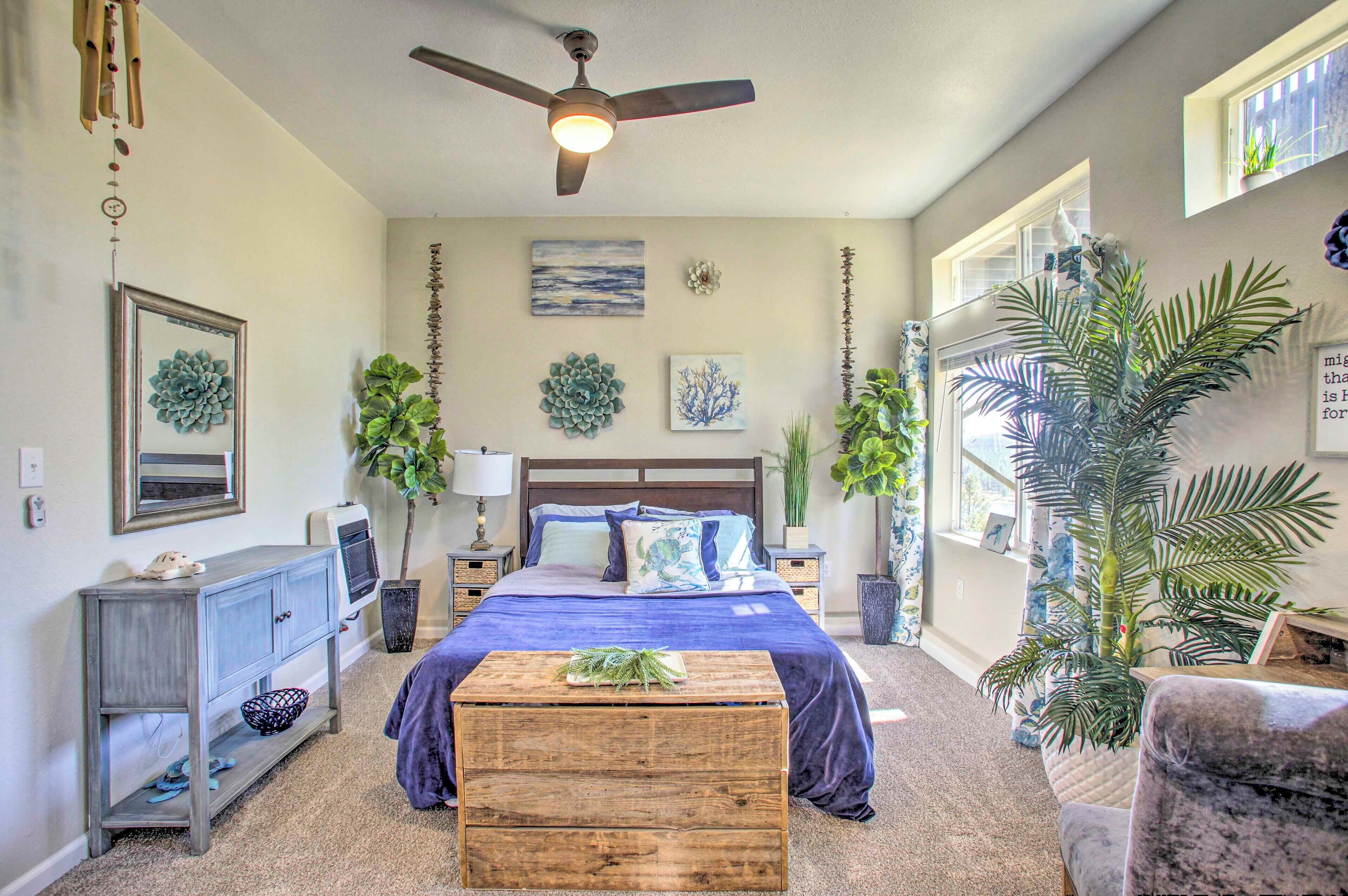 A bedroom with a bed, a ceiling fan, a wooden chest, and various plants.