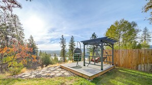 A wooden deck with a swing set and a pergola, surrounded by trees and a view of a lake. - Lakeview Lodge w/ Spacious Yard: Families Welcome (Nine Mile Falls)