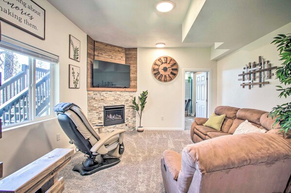 A living room with a stone fireplace, a mounted clock, and a large window. - Lakeview Lodge w/ Spacious Yard: Families Welcome (Nine Mile Falls)