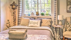A cozy bedroom with a large bed, a bedside lamp, a window with curtains, and a small table with a lamp. - Lakeview Lodge w/ Spacious Yard: Families Welcome (Nine Mile Falls)