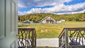 A view from a porch with a wooden railing, overlooking a grassy area with a barn and a fence. - Dog-friendly Huntsville Home, ATV Authorized Route (Huntsville)