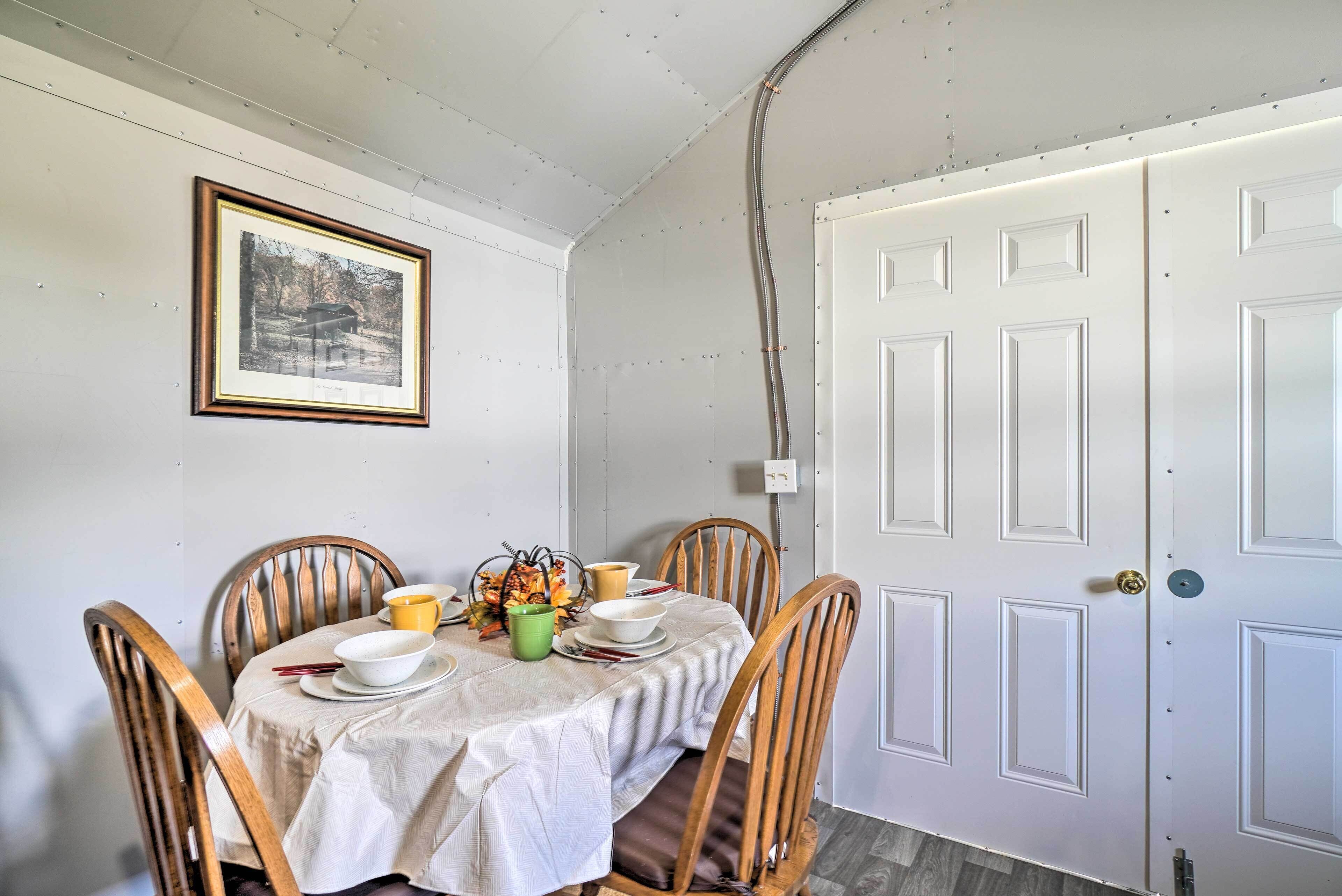 A dining area with a table set for four, wooden chairs, a framed picture on the wall, and a white door with a handle.