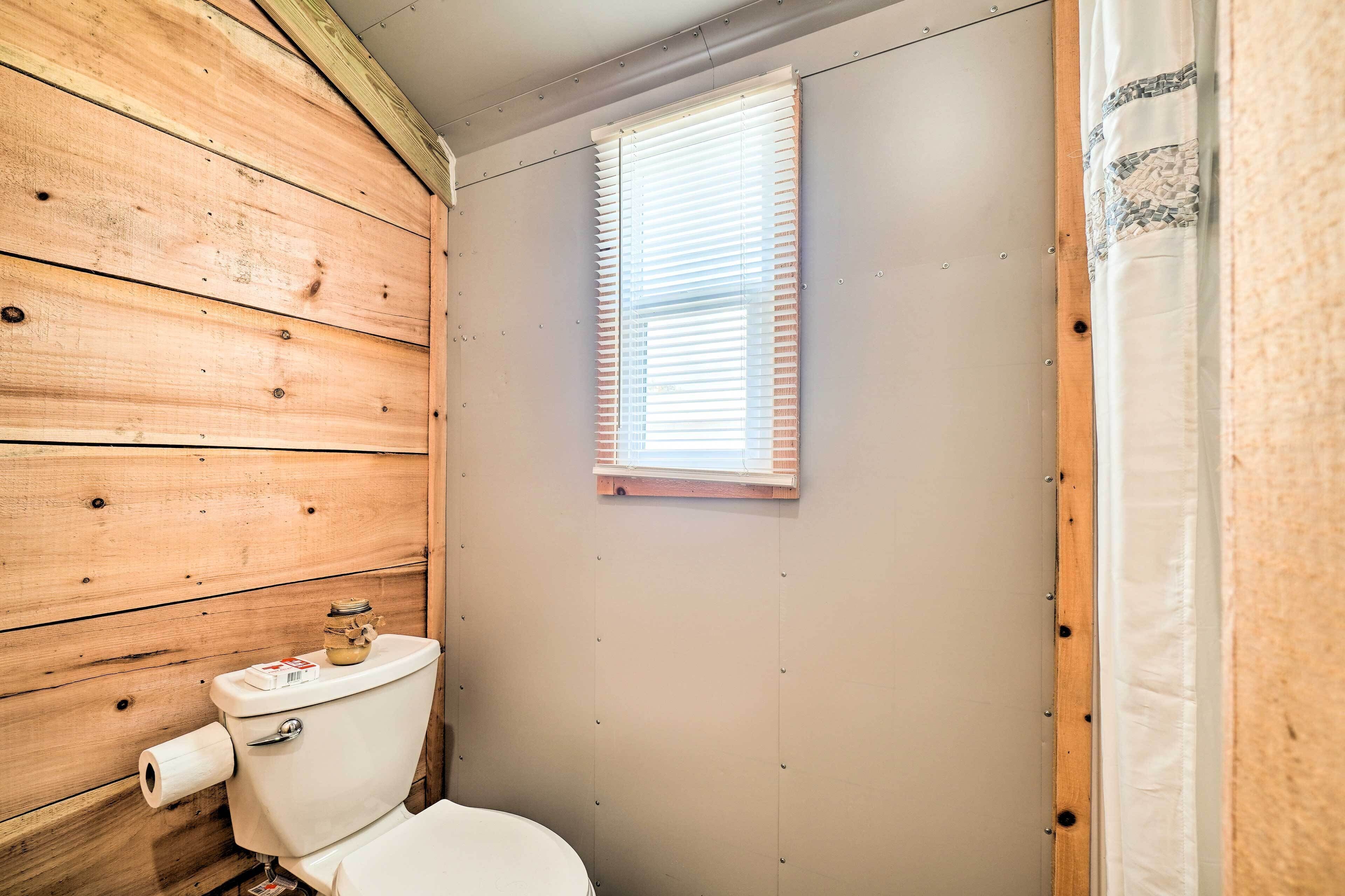 Ein Badezimmer mit Holzwandverkleidung, Toilette, einem Fenster mit Jalousien und einer Duschvorhang.