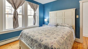 Een slaapkamer met een bed, nachtkastje, lamp en een raam met gordijnen.
