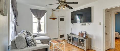 A living room with a ceiling fan, a TV mounted on the wall, a wooden coffee table, and a sofa with cushions.