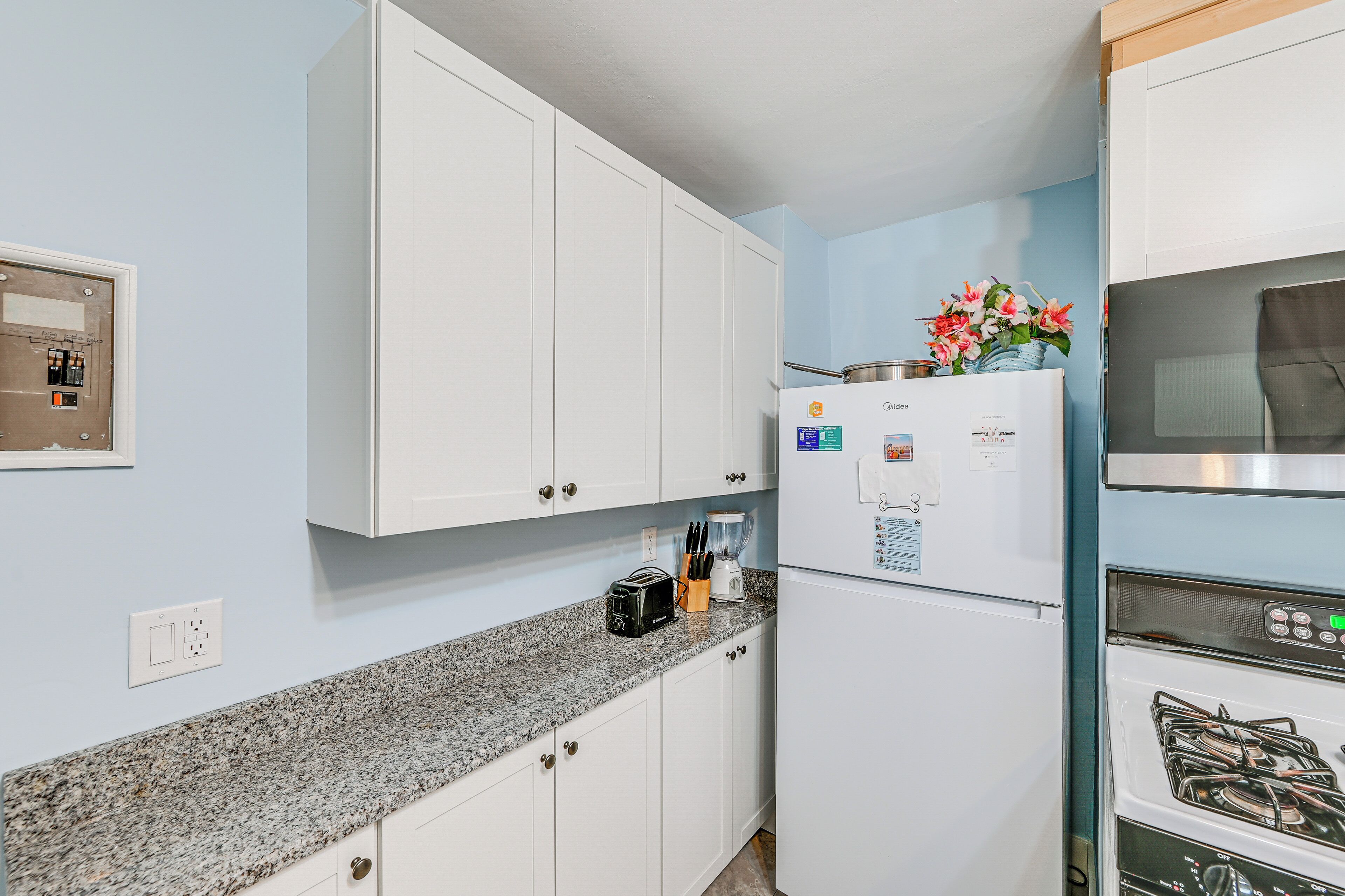 A kitchen with white cabinets, a granite countertop, a refrigerator, a stove, and a flower vase.