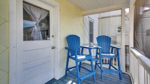 Een veranda met twee blauwe stoelen en een kleine tafel, een witte deur en een gele muur.