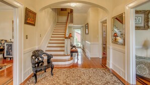 A grand hallway with a wooden staircase, ornate wall decorations, and a patterned rug. - Family Laurinburg Home w/ Private Yard & BBQ (Laurinburg)