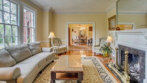 A spacious living room with a sofa, coffee table, and fireplace. A large window and door provide natural light and access to another room. - Family Laurinburg Home w/ Private Yard & BBQ (Laurinburg)