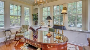 A spacious room with large windows, a wooden desk, a rocking chair, and a chandelier. - Family Laurinburg Home w/ Private Yard & BBQ (Laurinburg)