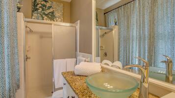A bathroom with a glass bowl sink, a shower, and a mirror with a patterned curtain.