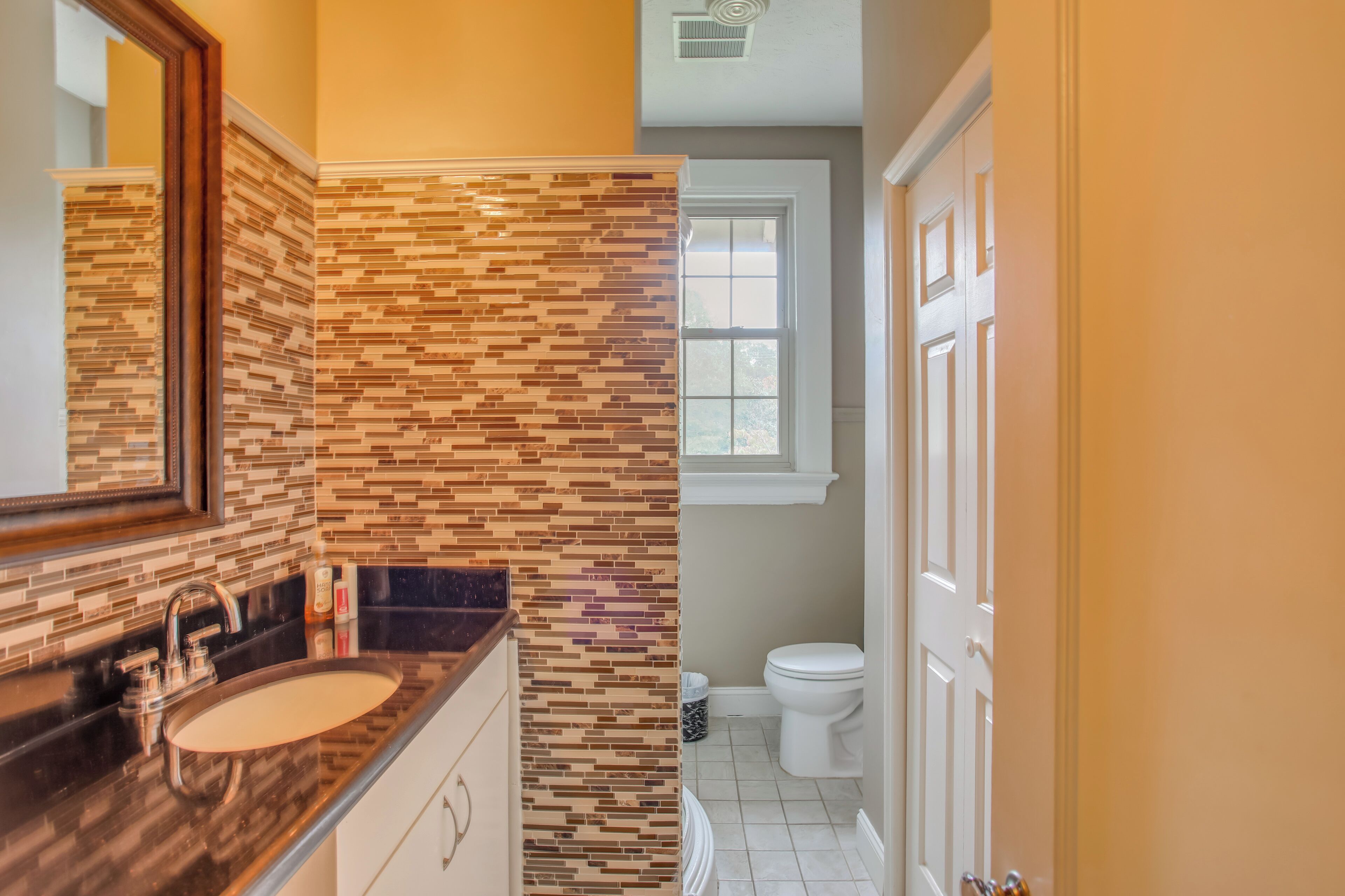 A bathroom with a tiled backsplash, a sink, a mirror, and a toilet.