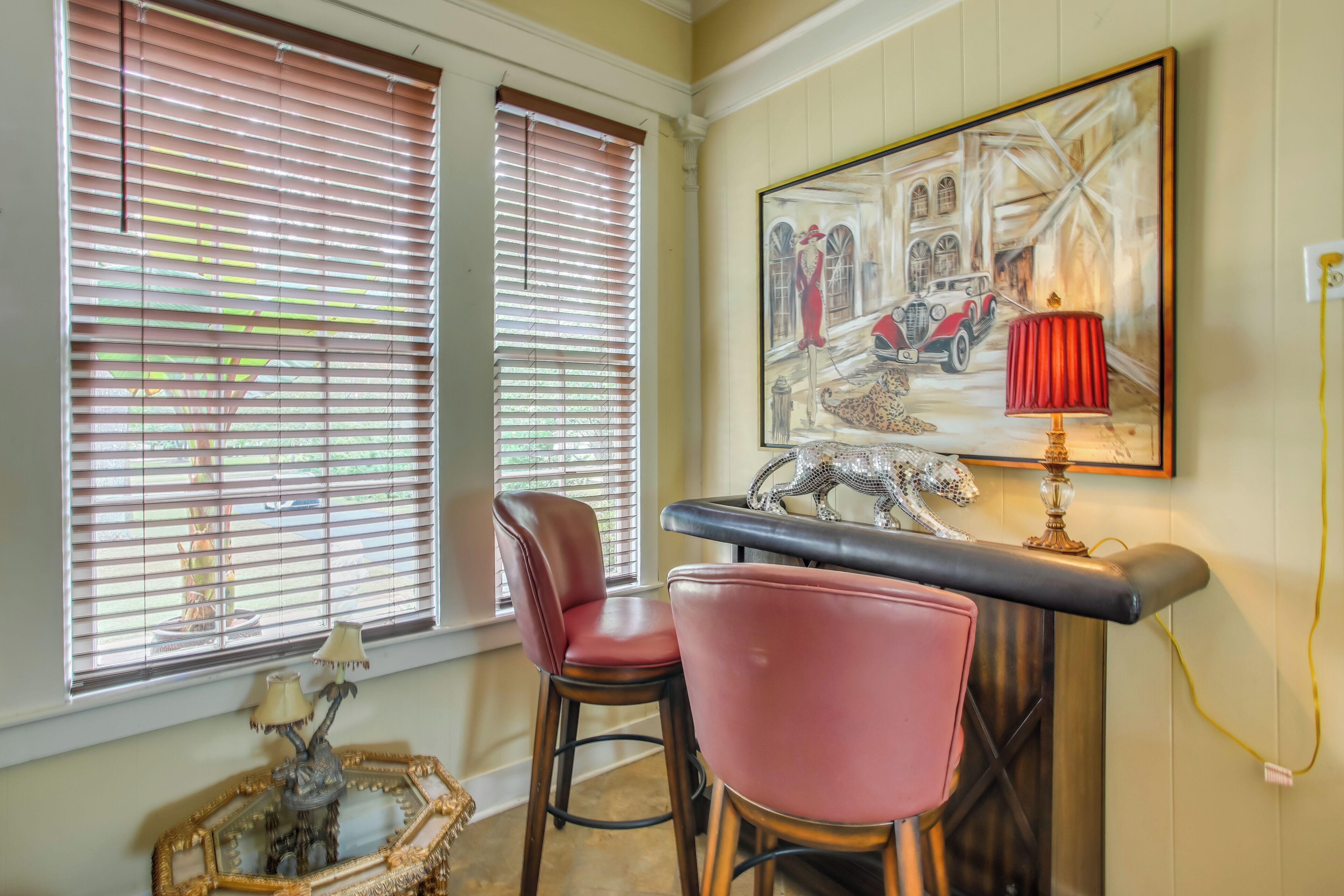 Een kamer met twee rode stoelen, een tafel met een lamp, en een schilderij van een klassieke auto en gebouwen.