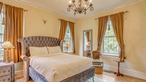 A bedroom with a large bed, a chandelier, a nightstand, a chair, and a small table. - Family Laurinburg Home w/ Private Yard & BBQ (Laurinburg)