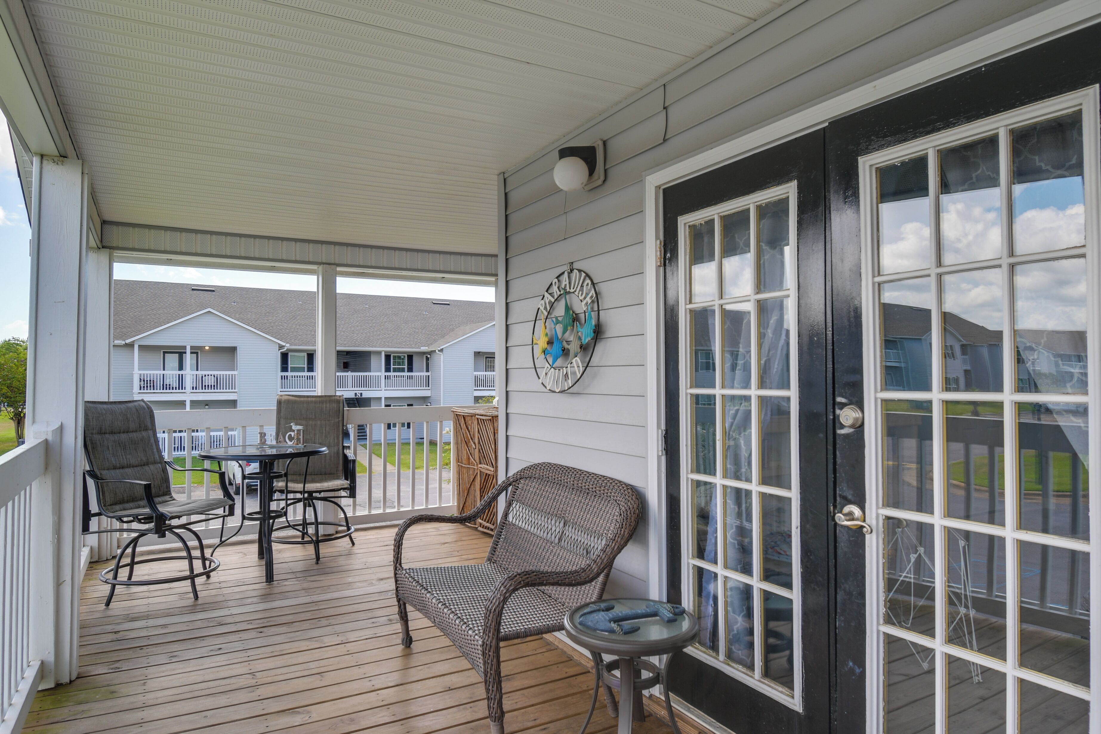 A covered porch with wicker furniture, a small table, and a decorative wall hanging.