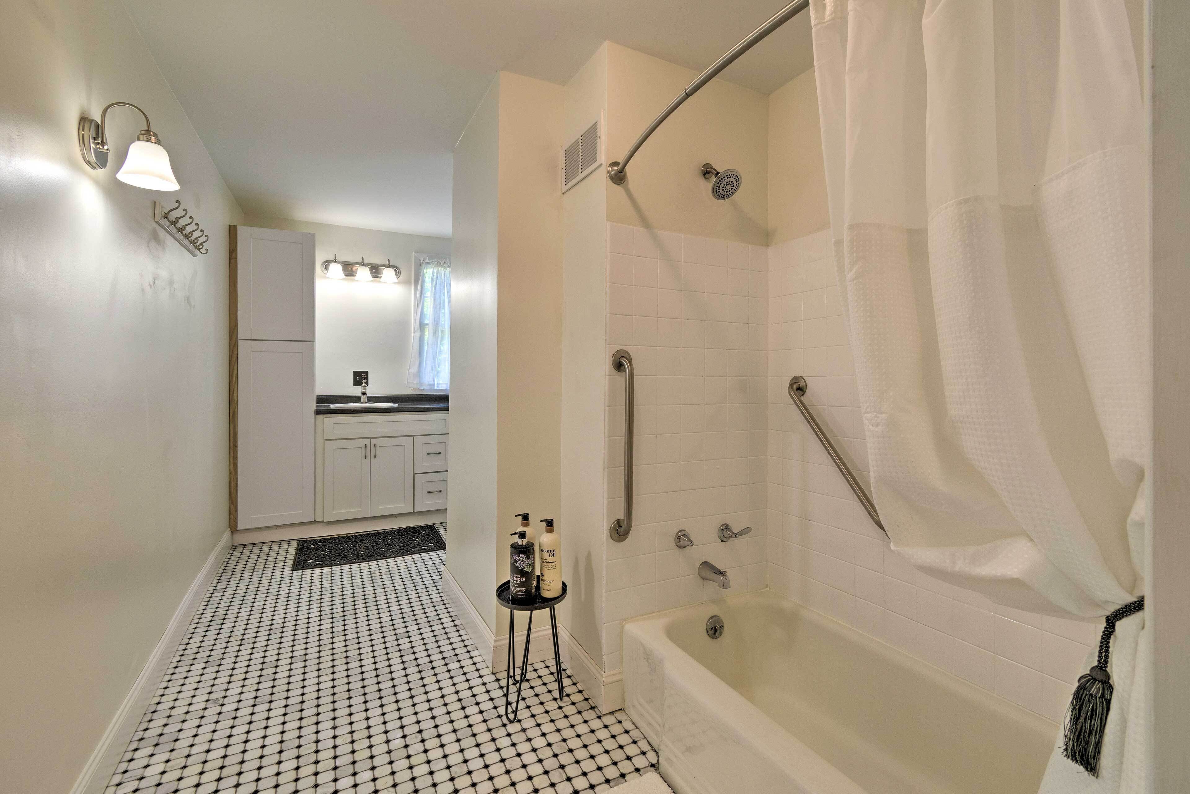 Un baño con bañera, ducha e inodoro. Hay una mesita con artículos de aseo.