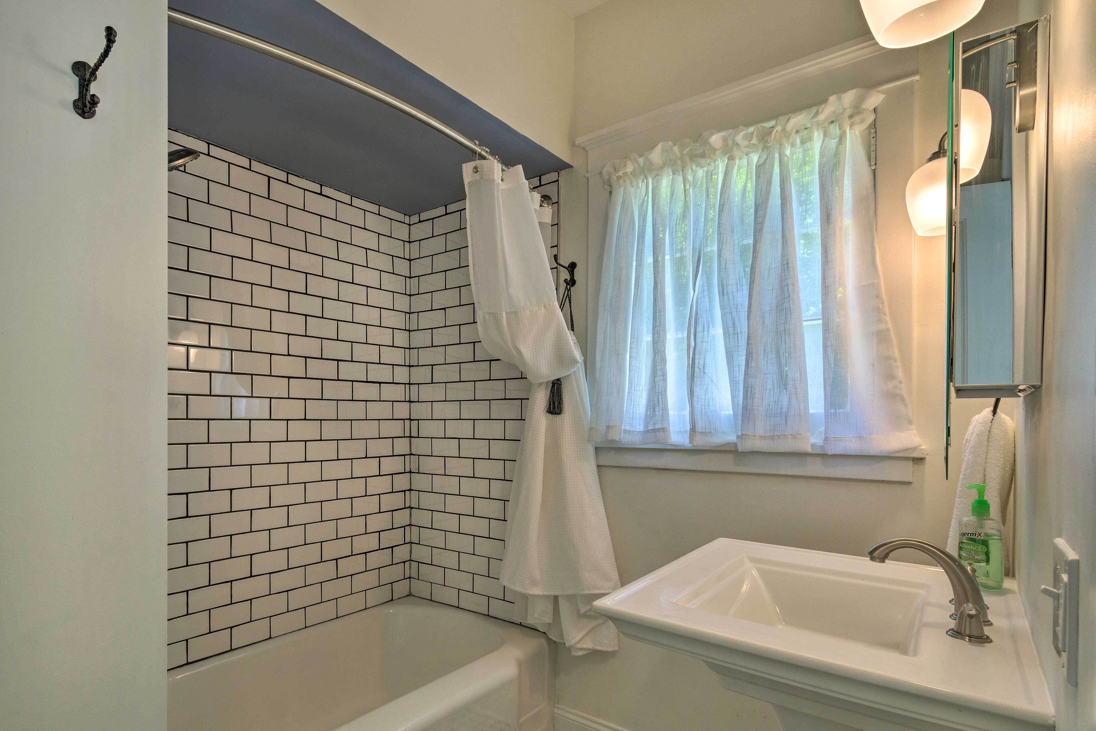 Une salle de bain avec un lavabo blanc, une douche avec un rideau blanc et une fenêtre avec des rideaux légers.