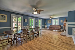 A dining area with a wooden table and chairs, a ceiling fan, and a blue wall with windows. - Sodus Point Historic Home ~ 1/2 Mi to Sodus Bay! (Sodus Point)