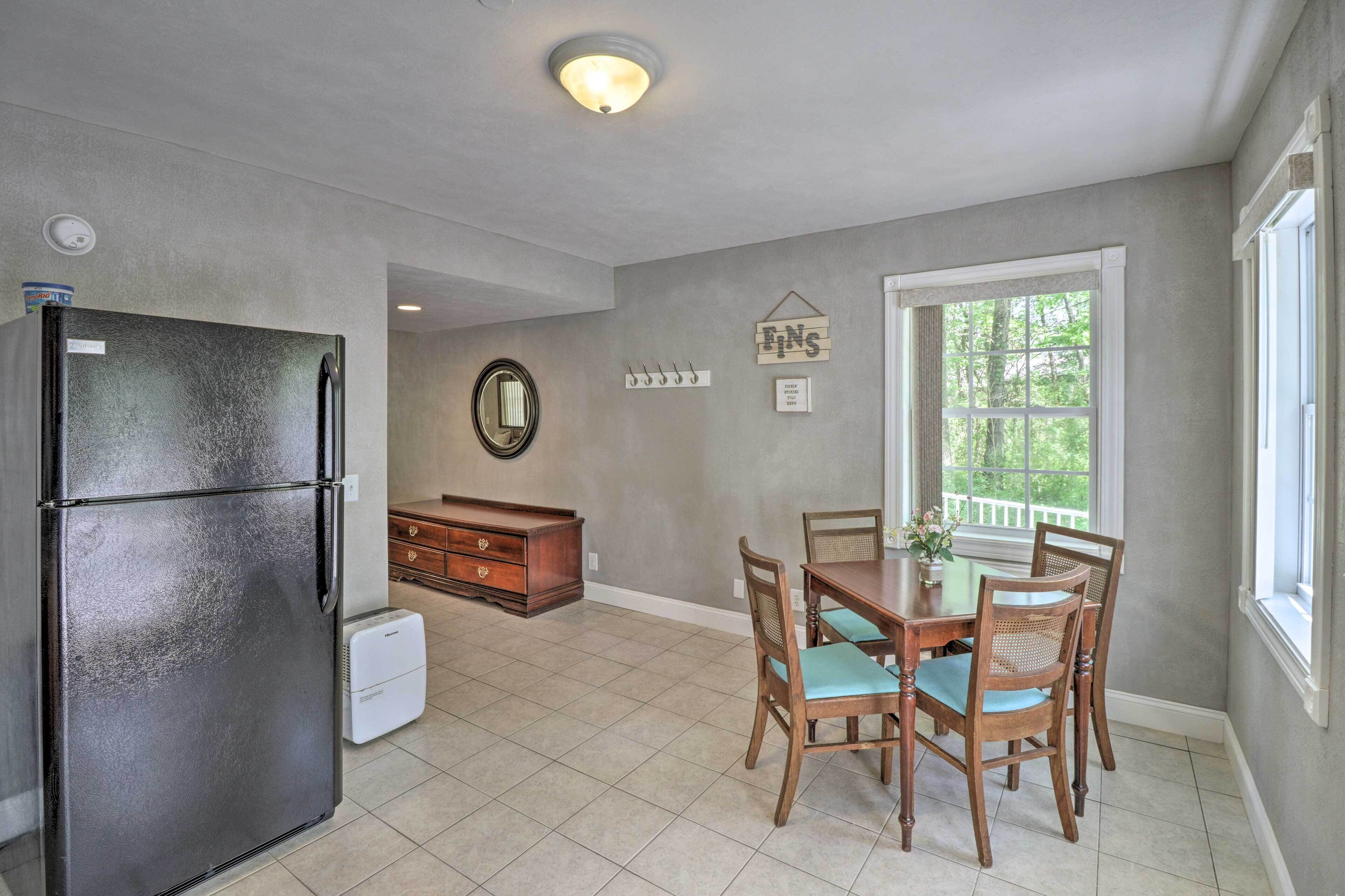 A kitchen with a refrigerator, a dining table with chairs, a window with a view, and a wall-mounted mirror.