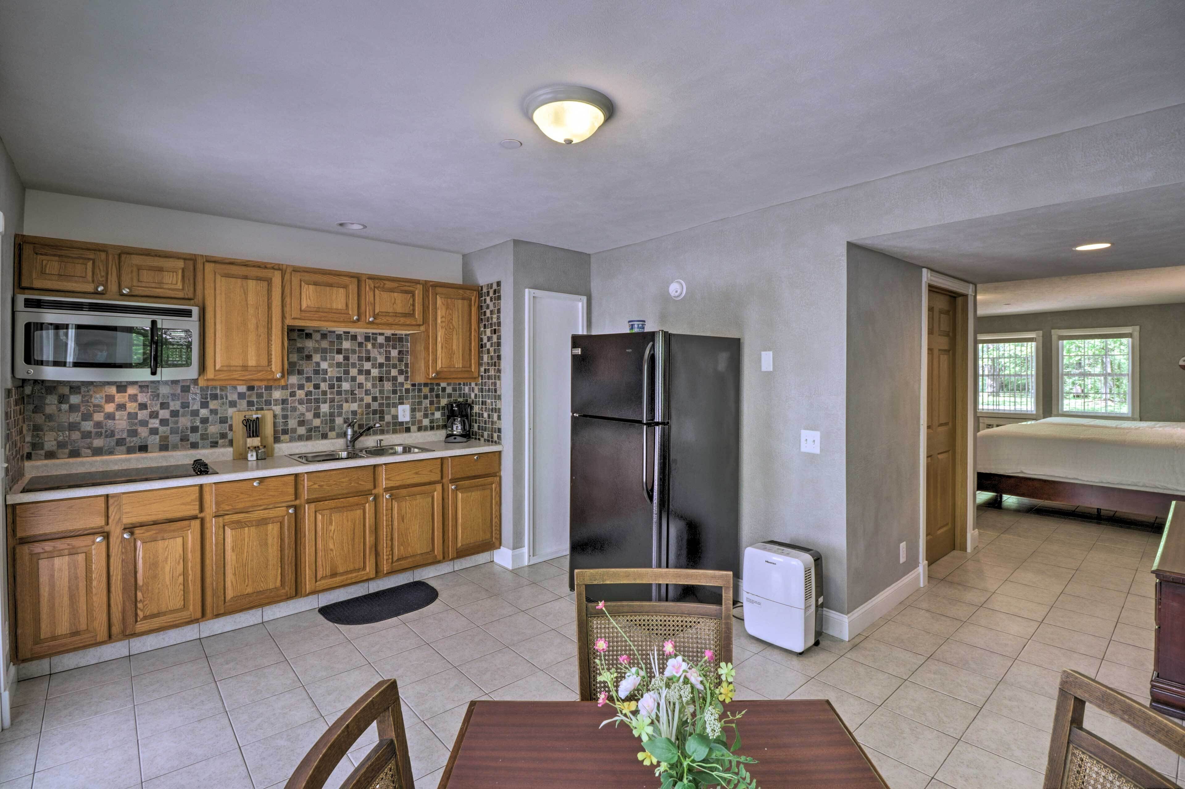 A compact kitchen with wooden cabinets, a microwave, a refrigerator, and a dining area with a table and chairs.