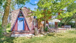 A cabin with a triangular roof, a blue door, and a patio area with a table and chairs. - 'snowflake Cabin' - Mins to Cody & Red Lodge! (Powell)
