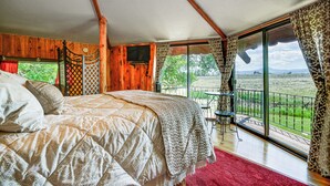 A bedroom with a large bed, wooden walls, a TV, and a balcony with a view of the countryside. - 'snowflake Cabin' - Mins to Cody & Red Lodge! (Powell)