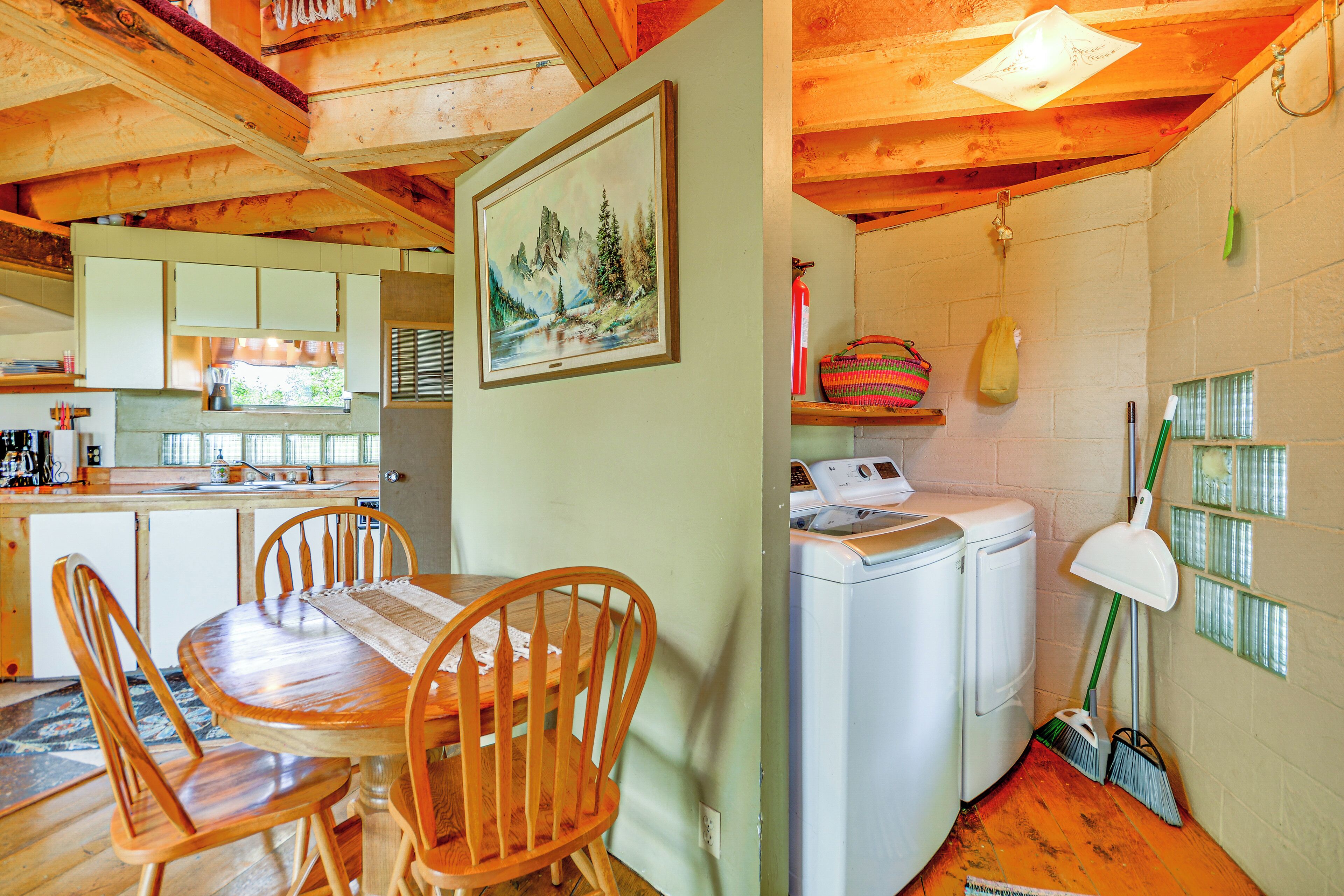A wooden dining table with chairs, a kitchen area with cabinets, a washing machine, and a broom.